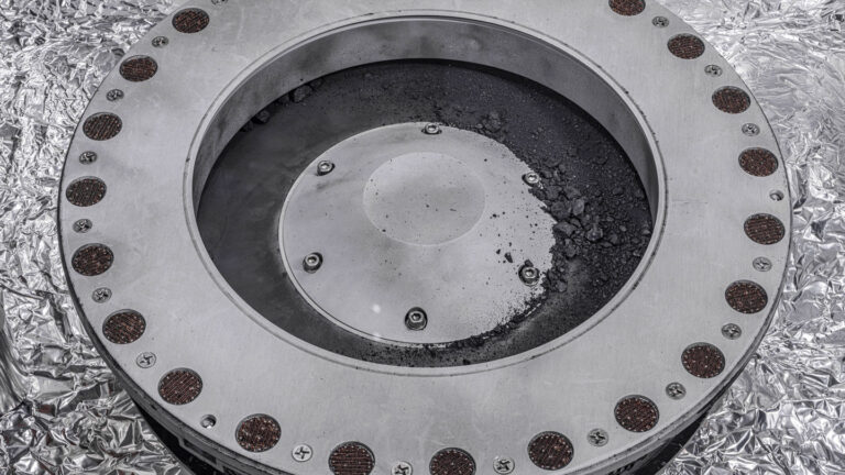 NASA’s first look at a sample from asteroid Bennu reveals life’s building blocks Asteroid rock and dust appears on the outer surface of the circular capsule that collected the asteroid sample.