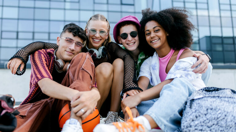 How to help transgender and nonbinary teens bloom during puberty a groupd of teens sitting outside a glass windowed building, the teens look young and happy