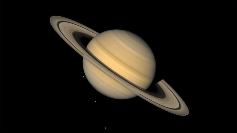 Saturn’s first Trojan asteroid has finally been discovered This image shows Saturn, ringed and in tones of tan, against an inky background. Three tiny light spots in the background and one dot against the lower half of the planet are four of Saturn