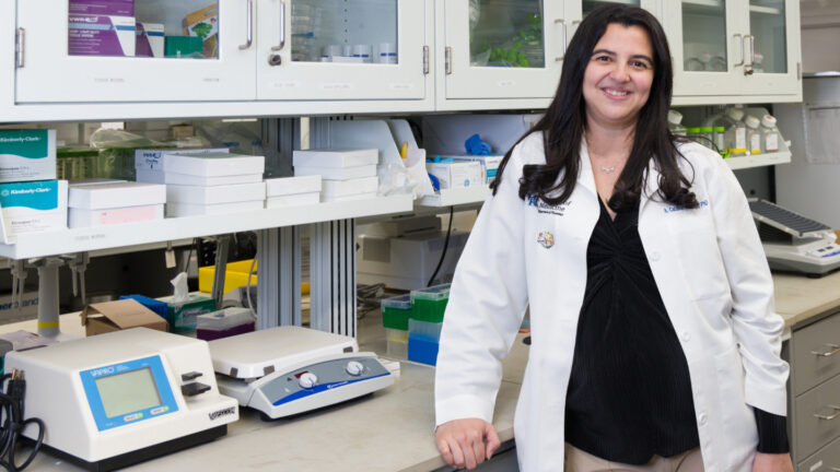 Dad’s backyard lessons inspired this hearing scientist to learn Hearing researcher A. Catalina Vélez-Ortega stands next to a counter with scientific machines. She is wearing a white lab coat and has black hair and fair skin. White shelves line the walls behind her.