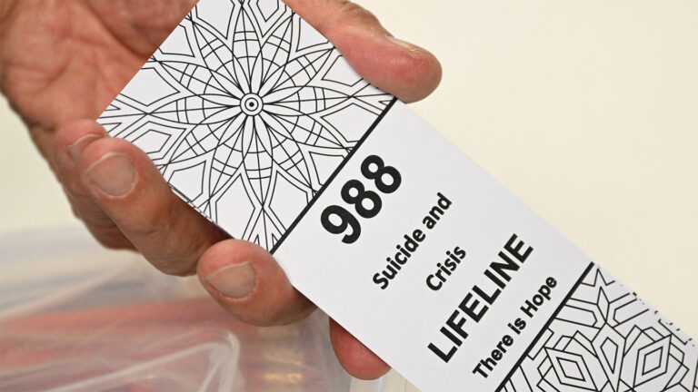 Federal cuts put help for mental health and drug addiction in peril A photo of a hand holding a card that reads "988 Suicide and Crisis Lifeline There is Hope"