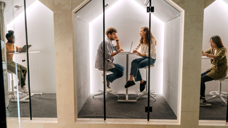 This microphone picks up sounds by watching them three glass-enclosed cubicles with young professionals in each. The middle cubicle has two people in a discussion