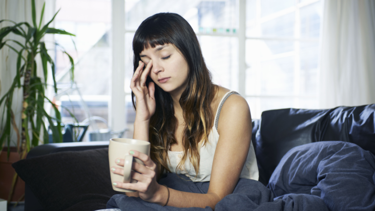 Scientists Say: Chronohygiene a teen girl sits on a couch holding a mug, sleepily rubbing one of her eyes